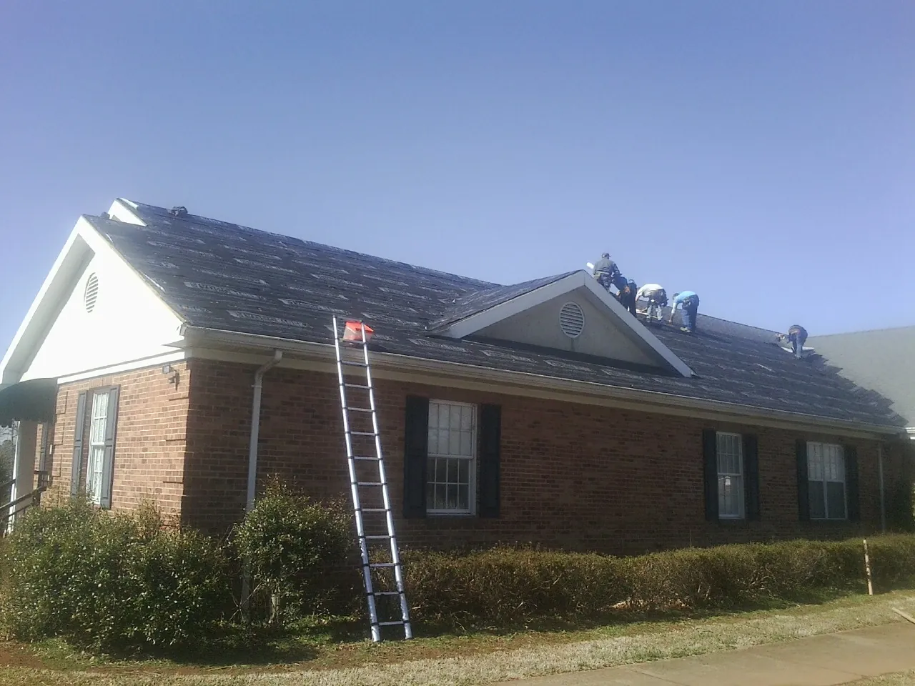 Crew tearing shingles off a brick ranch roof with a ladder set — Metal Roof Repair work by our crew in Vinton