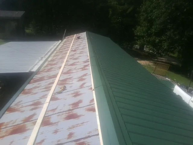 Old rusted panels beside newly installed green metal roofing — Wind Damage Roof Repair by Roofing Brothers in Vinton