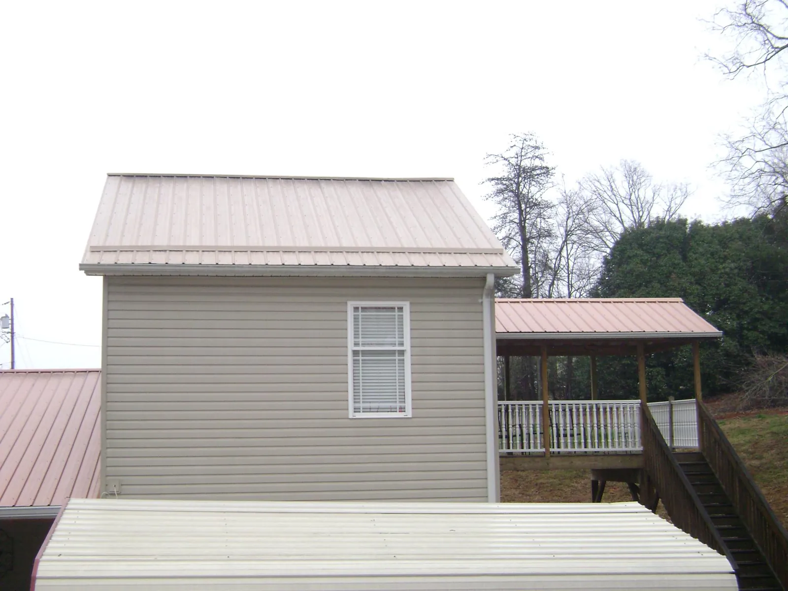 Tan metal roofs on a two story addition and attached porch, from a Roof Replacement job in Vinton